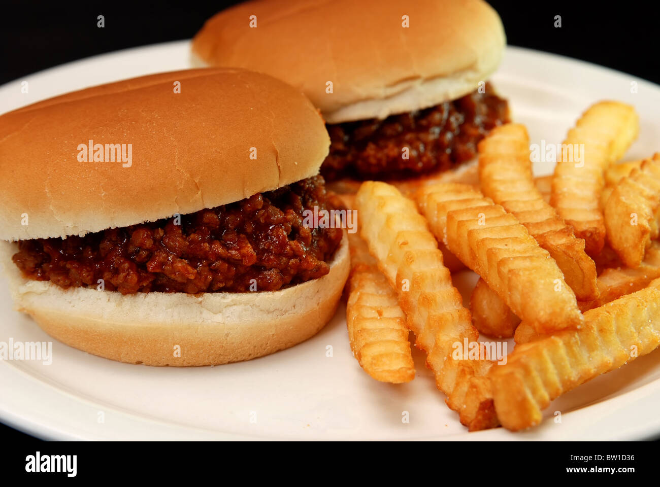 Two sloppy joe burgers and crinkle cut french fries isolated on black