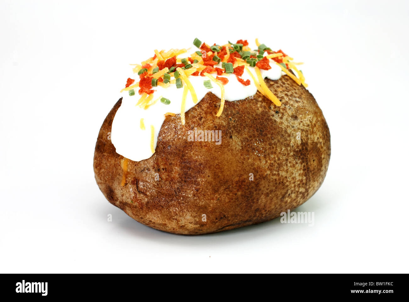 Baked potato loaded with butter, sour cream, cheddar cheese, bacon bits, and chives. Isolated on white background. Stock Photo