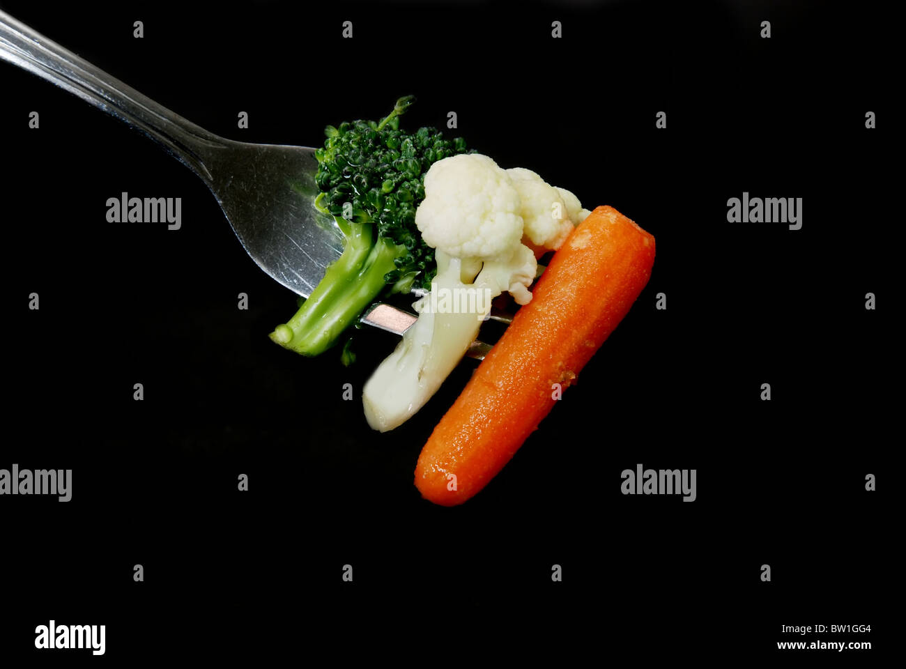 Broccoli, cauliflower, and carrot on fork isolated on black background. Stock Photo