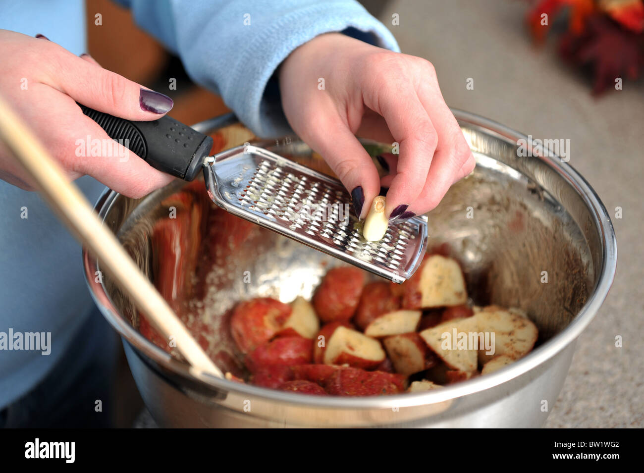 Woman grating garlic over red skin potatoes for dinner Stock Photo