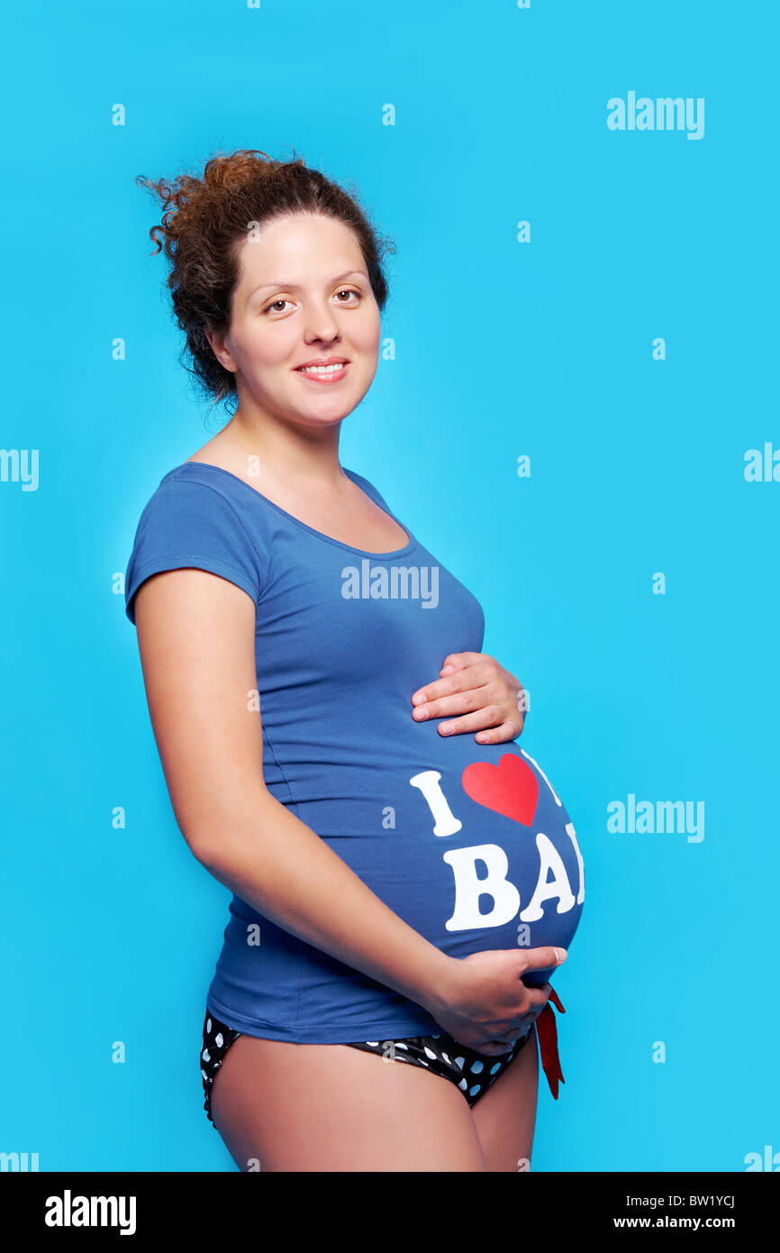 Portrait Of Pretty Pregnant Woman Touching Her Stomach And Looking At Camera Over Blue 