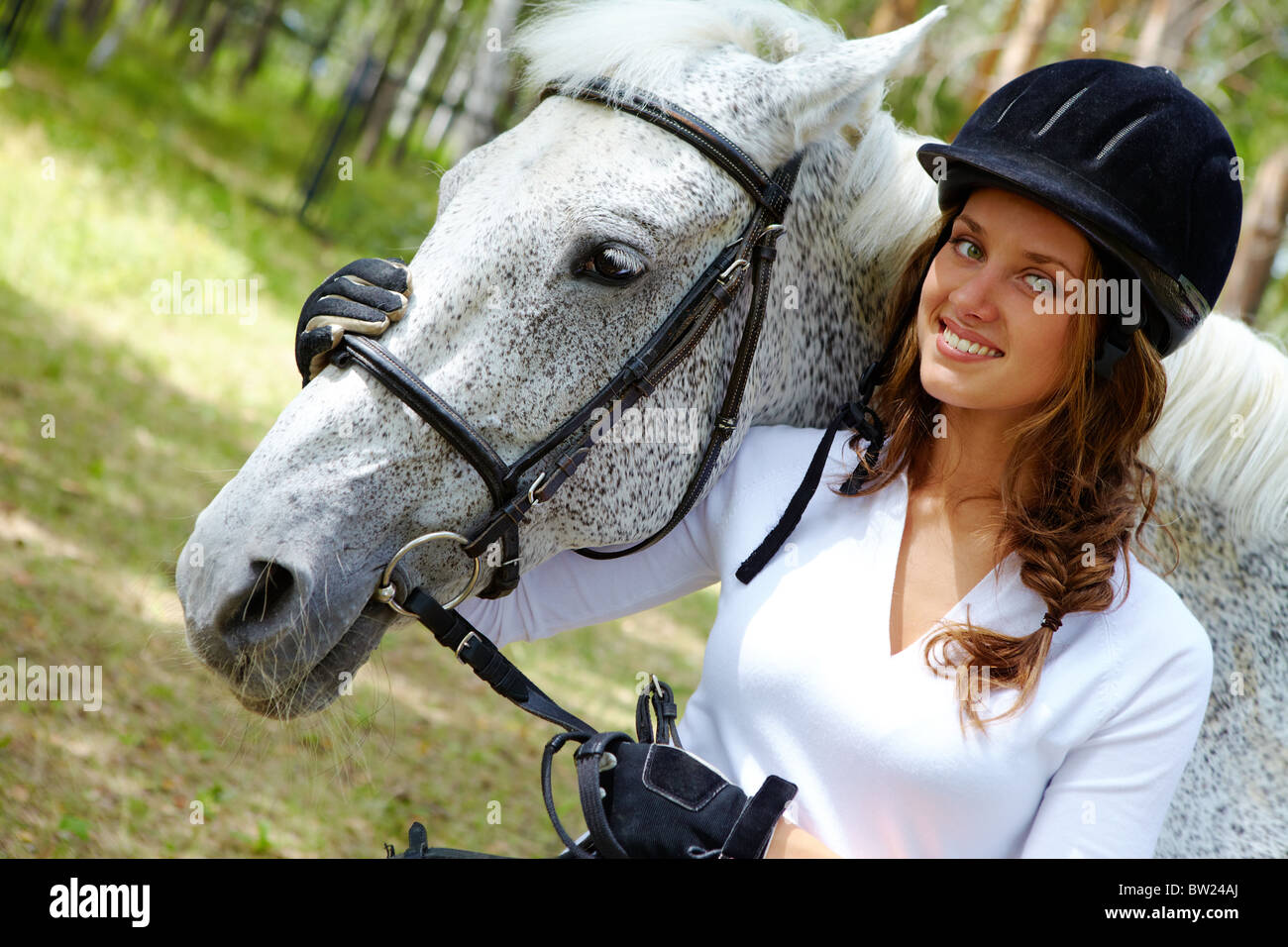 Image of happy female in riding cap embracing purebred horse and