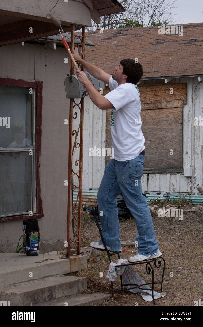 College student belonging to Filipino-American campus group paints a run-down house in a low-income neighborhood in Austin Texas Stock Photo