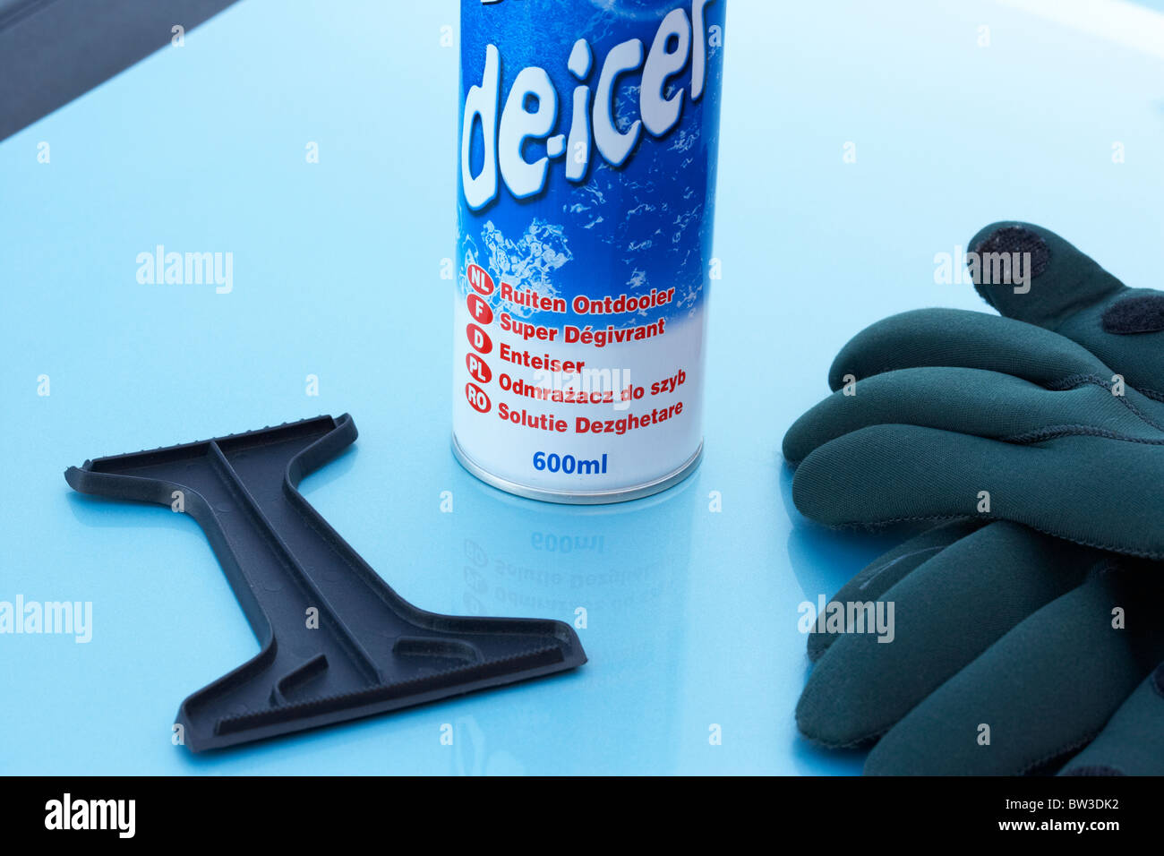 can of de-icer ice scraper and gloves on a car bonnet Stock Photo