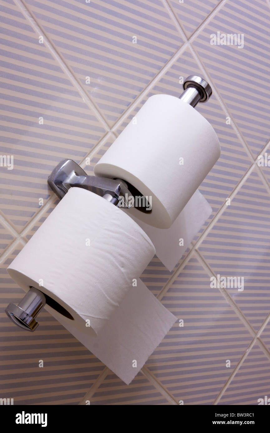 Twin toilet roll dispenser in a hotel room with striped tiles behind Stock Photo