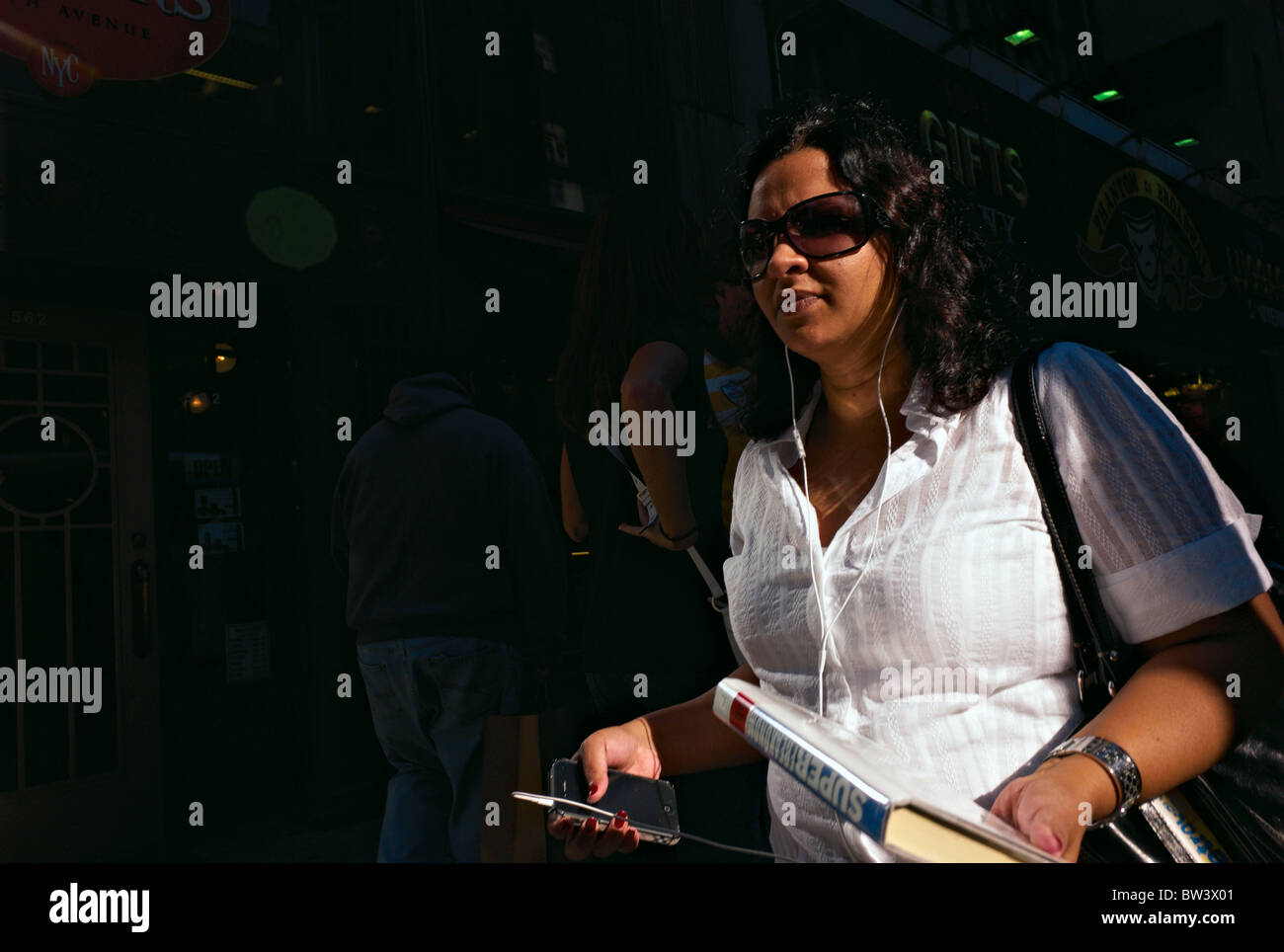 Woman in sunglasses walking on sidewalk while holding smart phone Stock Photo