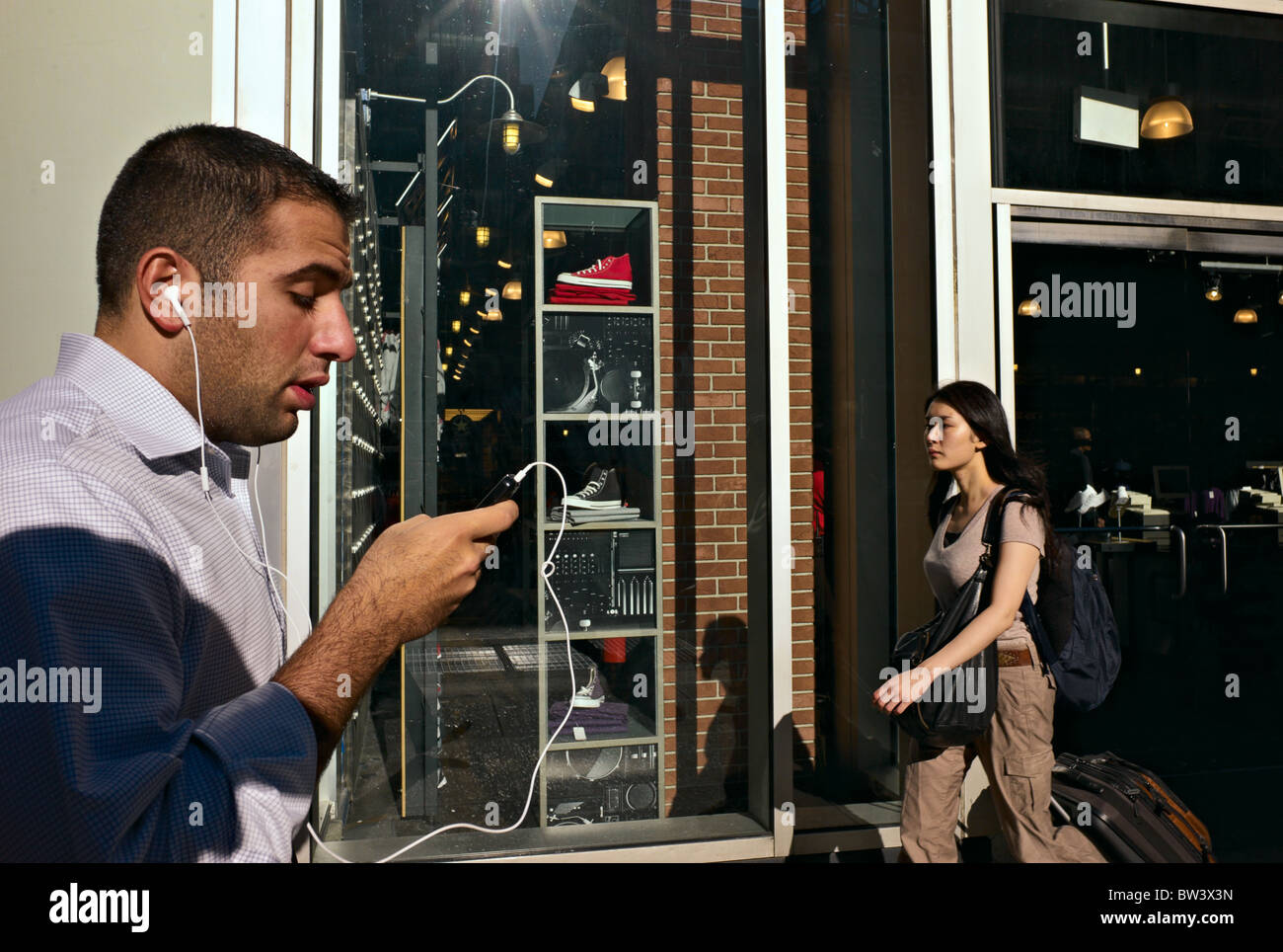 Man walking while operating hand-held device and wearing ear phones. Stock Photo