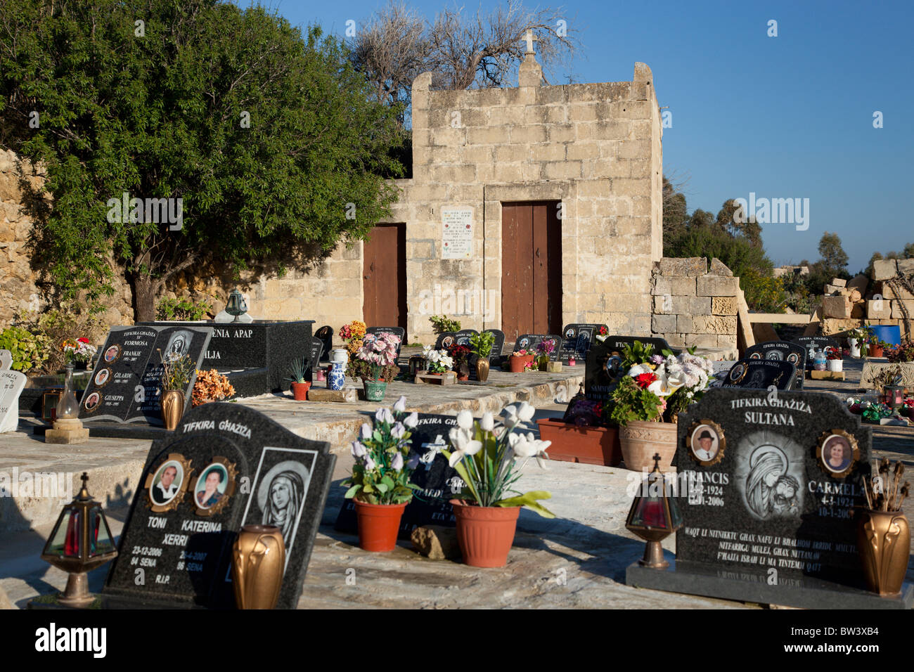Restrained stone chapel and marble plagues and flower arrangements set on graves in a cemetery in the Maltese Islands. Stock Photo