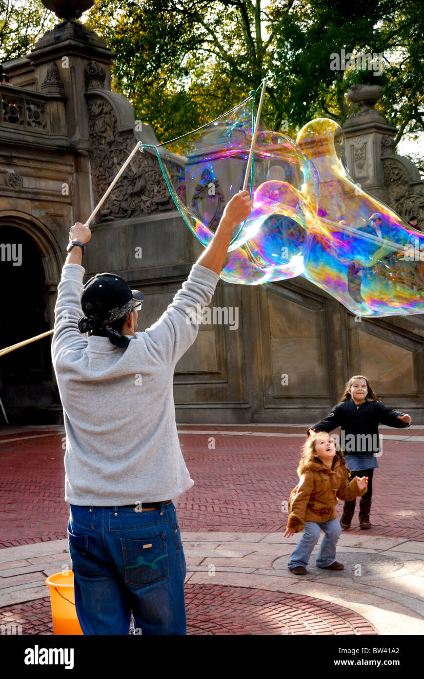 A man creating very large bubbles entertains two young girls in