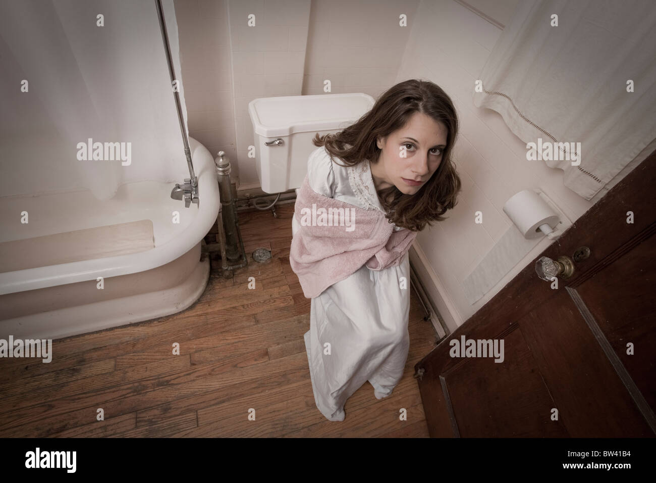Young woman in a nightgown and a towel sitting on the edge of her toilet Stock Photo