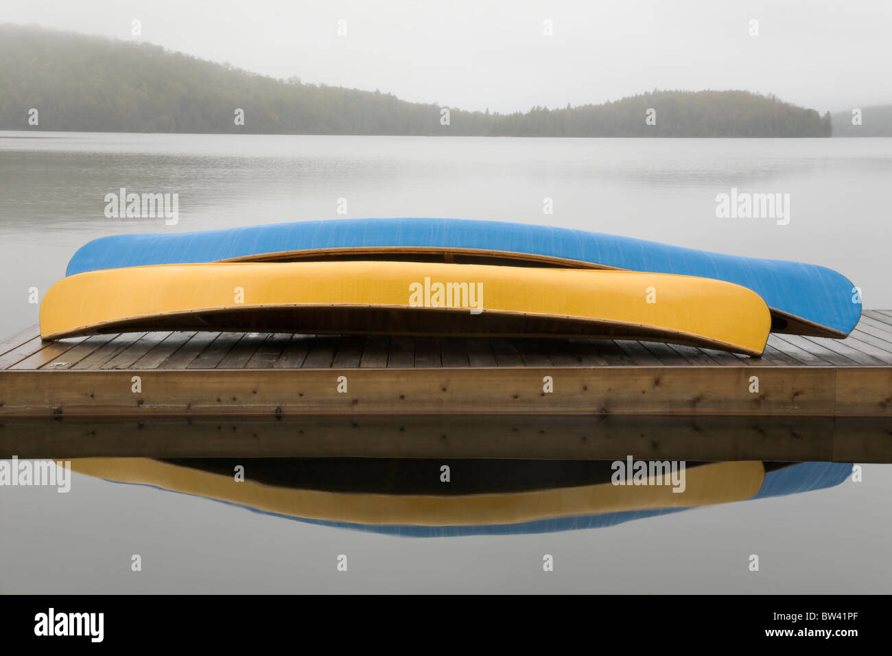 Blue and yellow canoes on cottage dock on a misty morning, Algonquin Park, Ontario Stock Photo