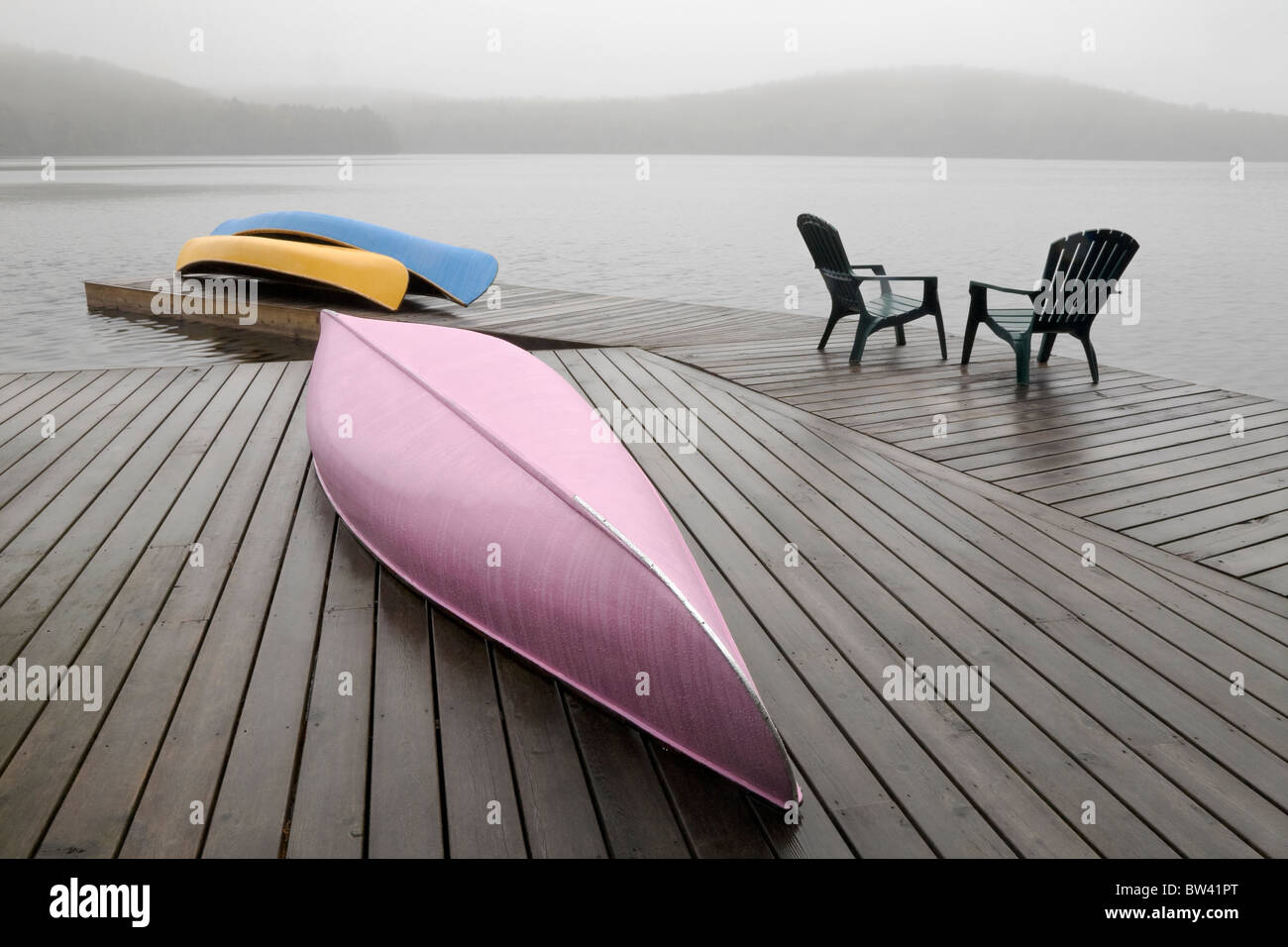 Colourful canoes and chairs on dock on a misty morning, Algonquin Park, Ontario Stock Photo