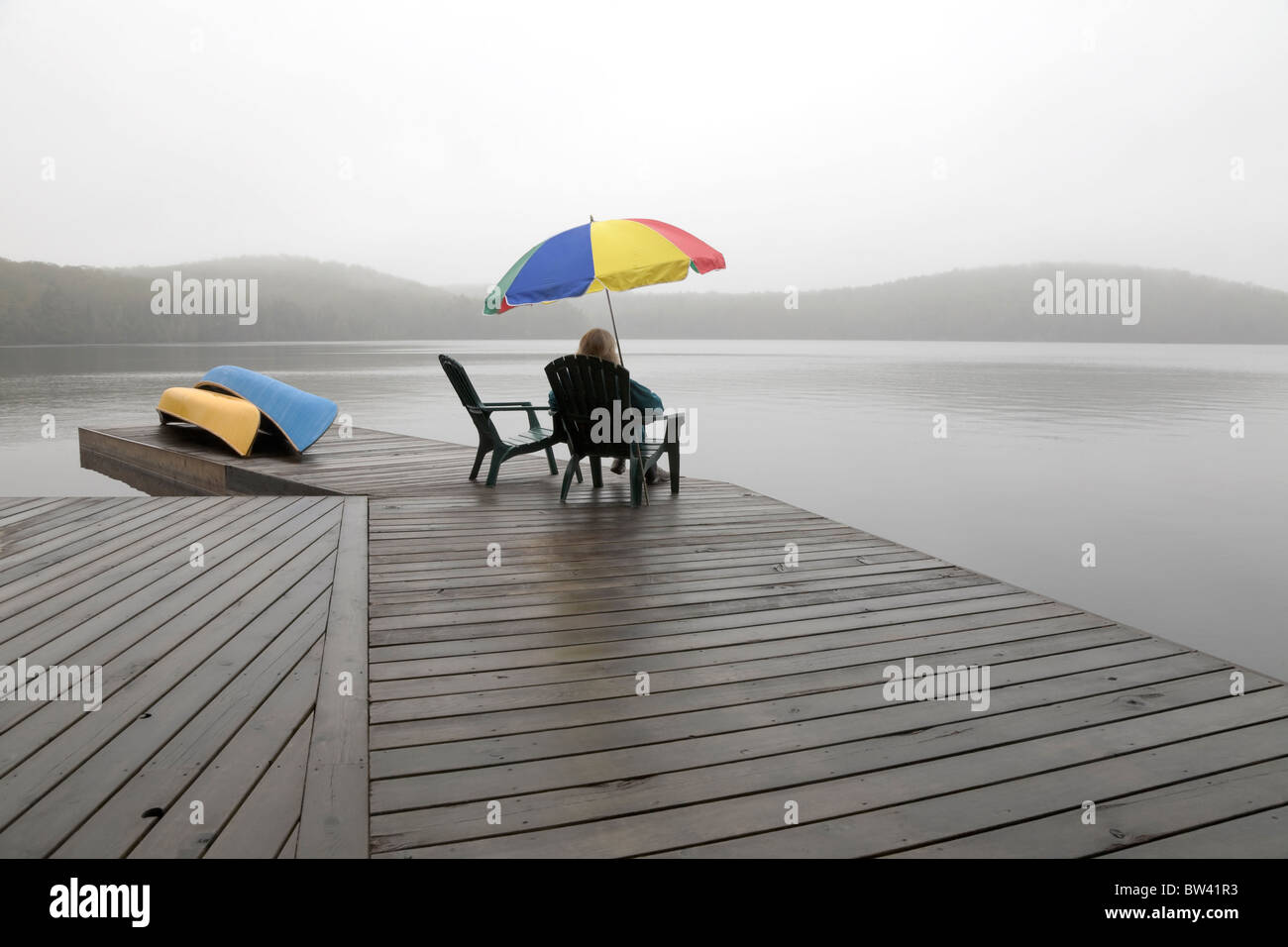 Senior woman on a cottage dock on a misty morning, Algonquin Park, Ontario Stock Photo