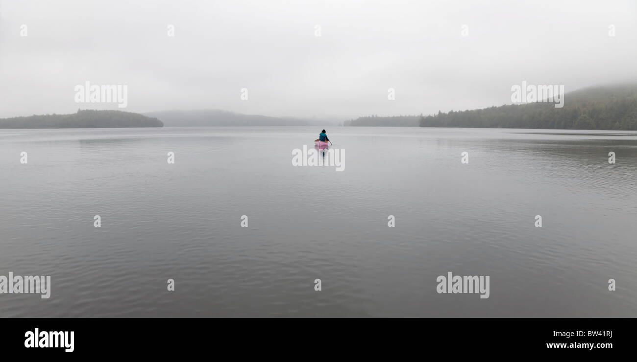 Senior woman canoeing solo on a misty morning, Algonquin Park, Ontario Stock Photo
