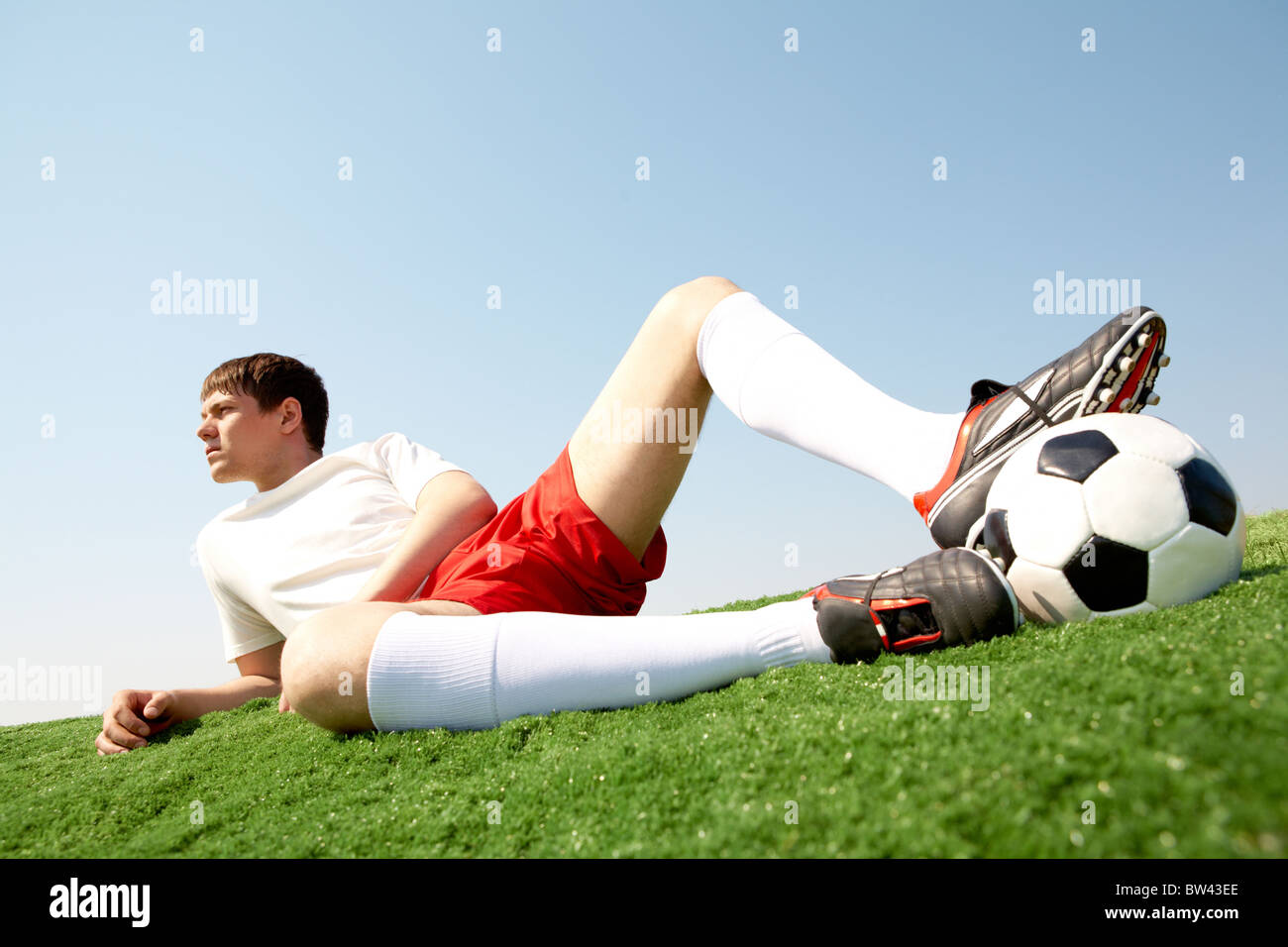 Photo of pensive soccer player lying on green grassfield and resting
