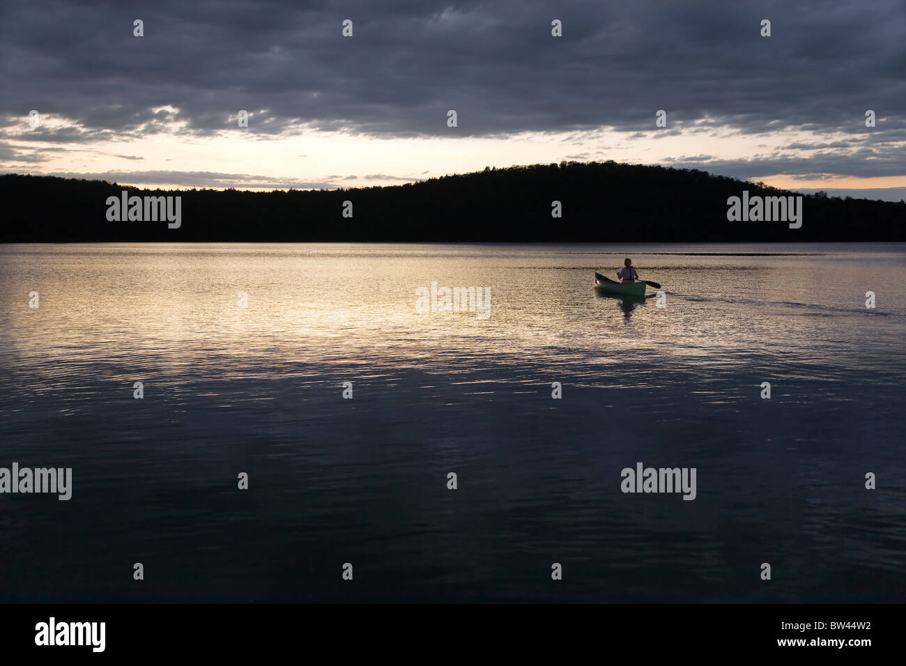 Woman canoeing solo at sunset, Algonquin Park, Ontario Stock Photo