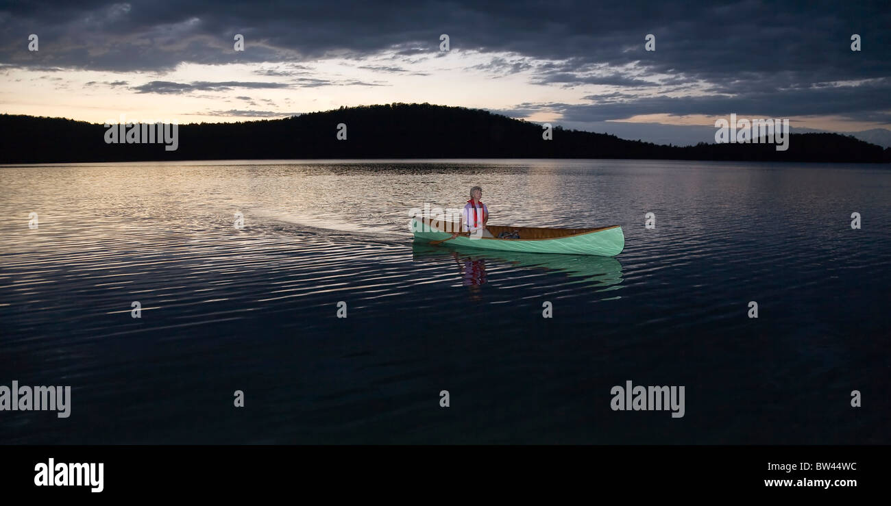 Senior woman canoeing solo at sunset, Algonquin Park, Ontario Stock Photo