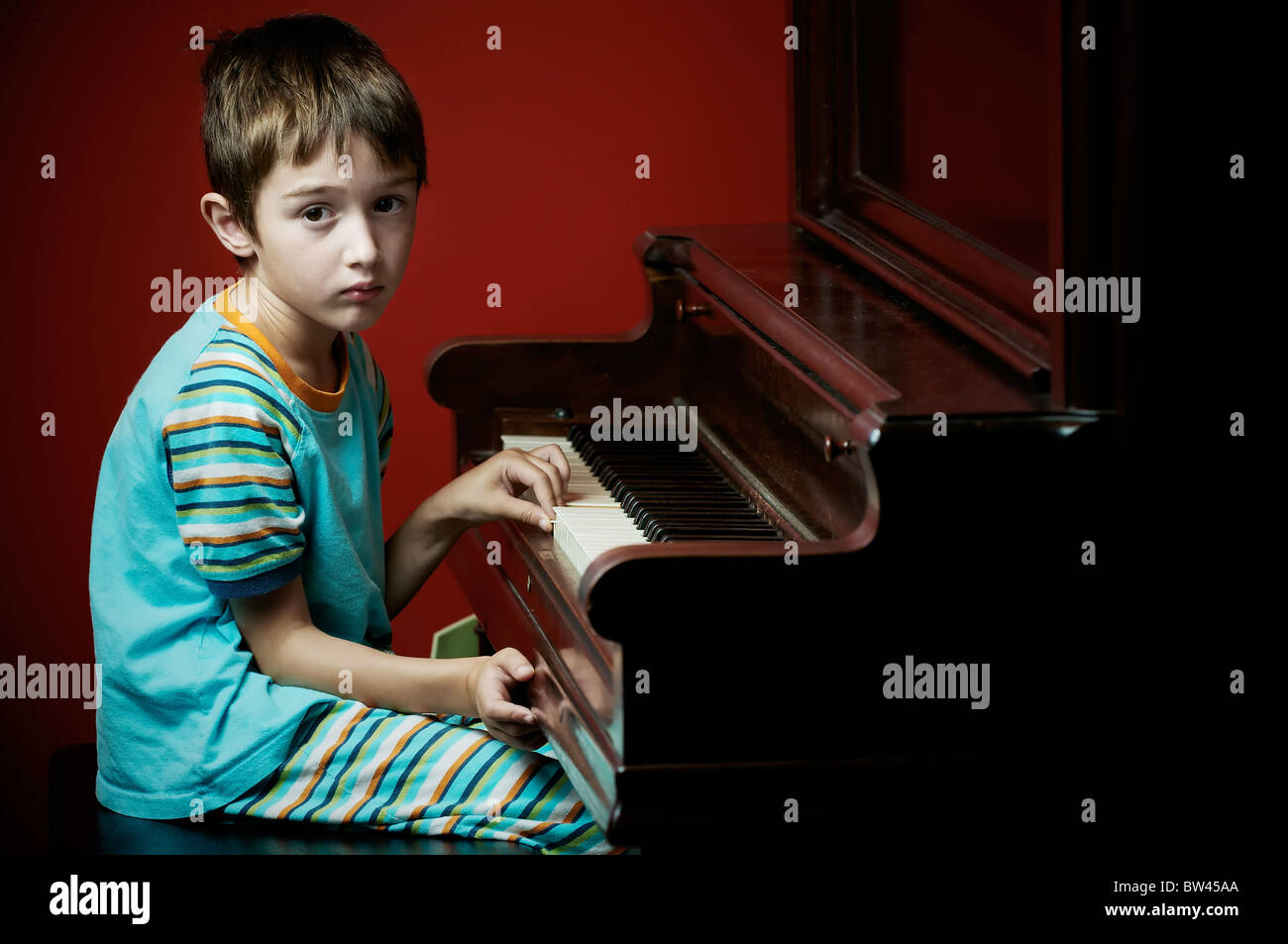 Young boy sitting at an old piano looking bored Stock Photo Alamy