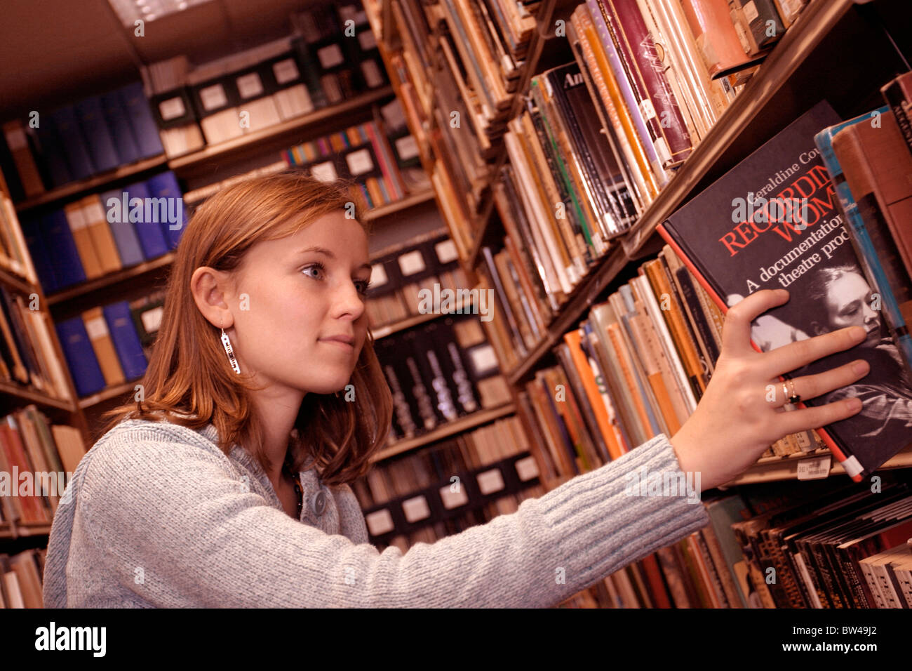 Young woman looking through books on library shelves. Librarian