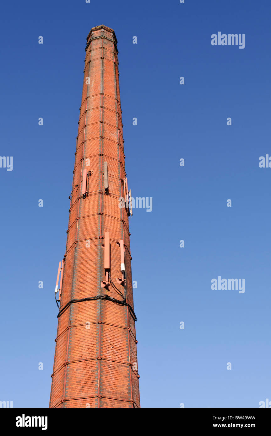 Tall red-brick chimney, common at 19th Century Irish linen mills, with mobile phone antennas Stock Photo