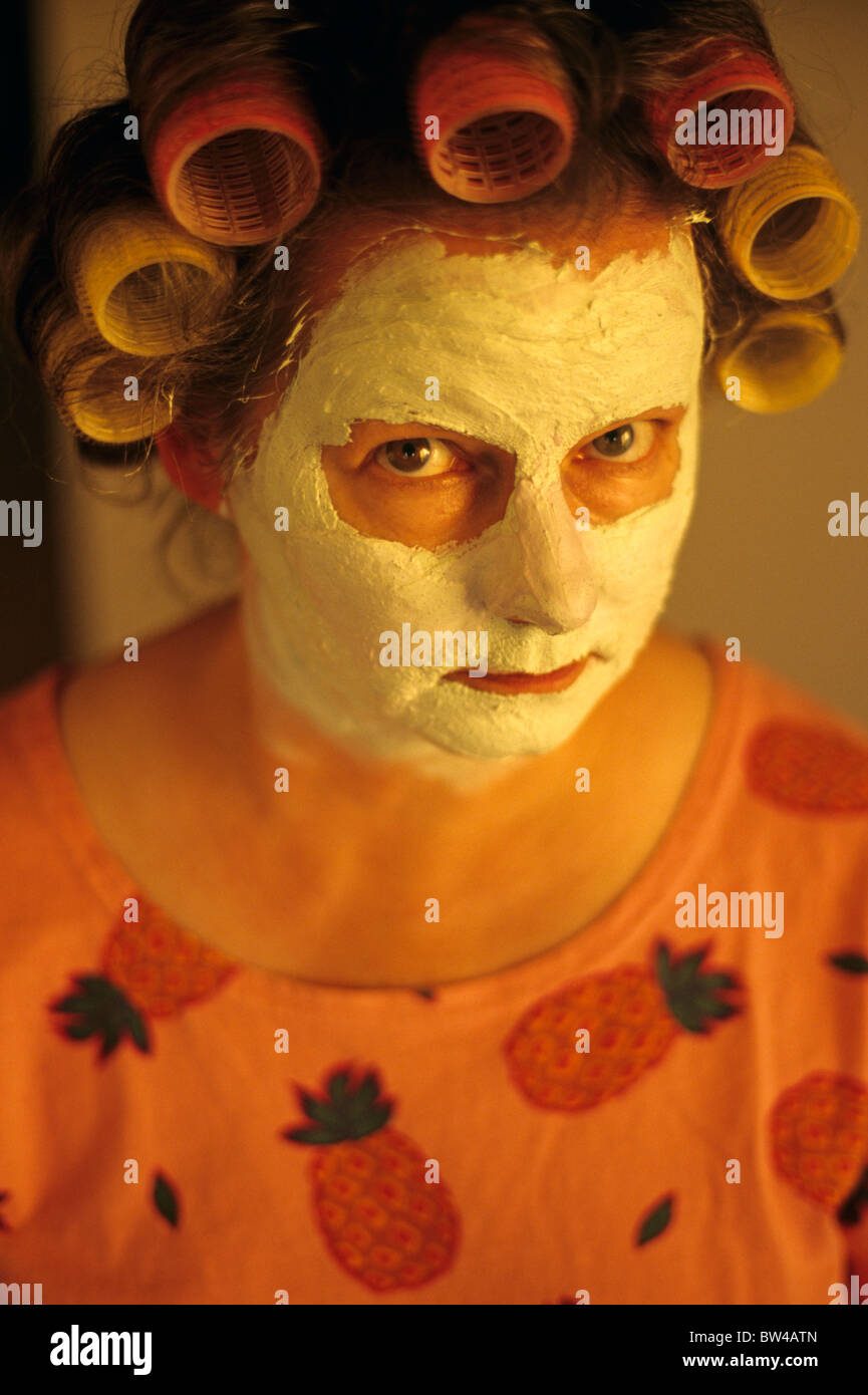 Woman, mother at dining room table with facial mask and hair in curlers looking into camera, Marysville, Washington USA MR Stock Photo