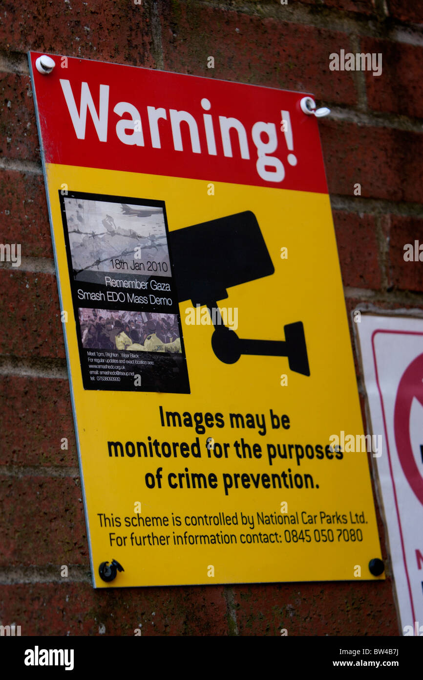 Warning of CCTV cameras outside a carpark in Brighton, East Sussex, UK. The sign has a Smash EDO Mass Demo sticker stuck to it. Stock Photo
