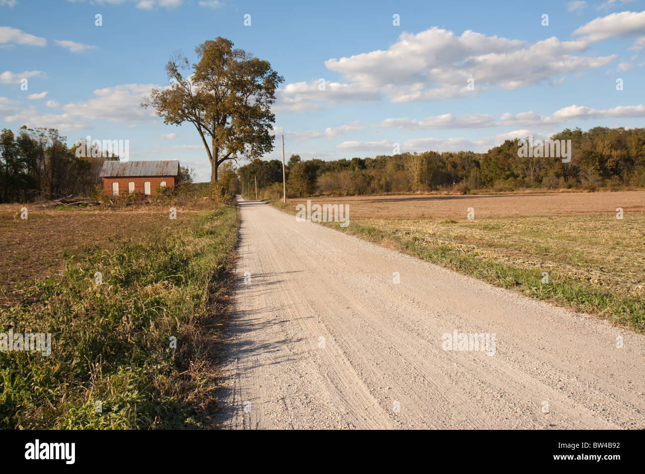 Abandoned on-room schoolhouse on a rural, gravel road in Indiana with a large tree, bright blue sky and clouds Stock Photo