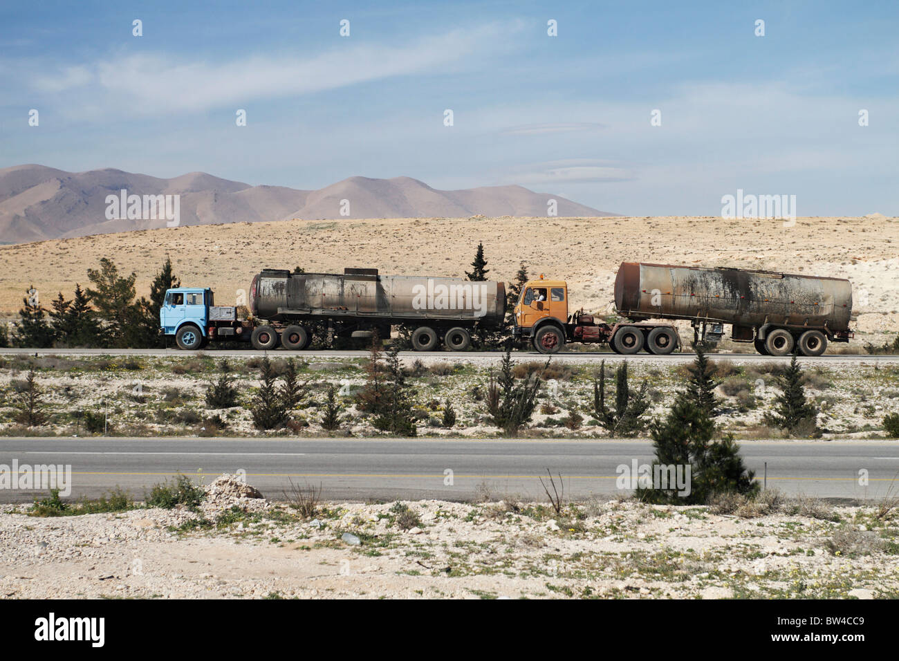 Two trucks driving across desert road in Syria. Stock Photo