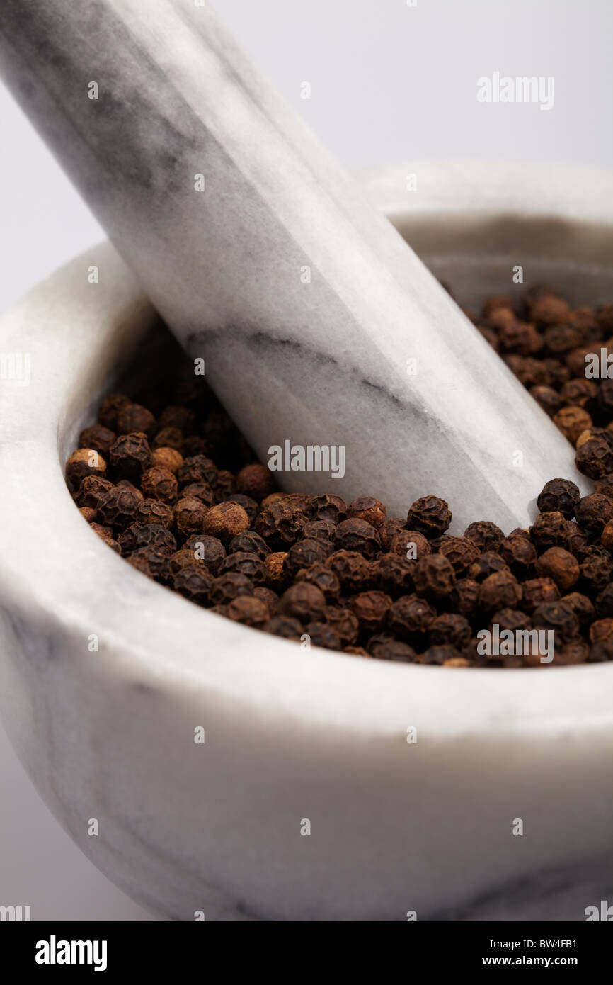 Grey and white pestle and mortar filled with black hot spicy peppercorns Stock Photo