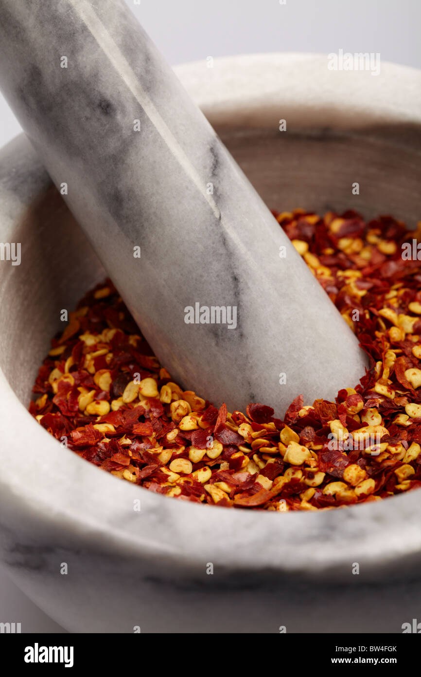 Grey and white pestle and mortar filled with red and yellow hot spicy dried chilli flakes Stock Photo