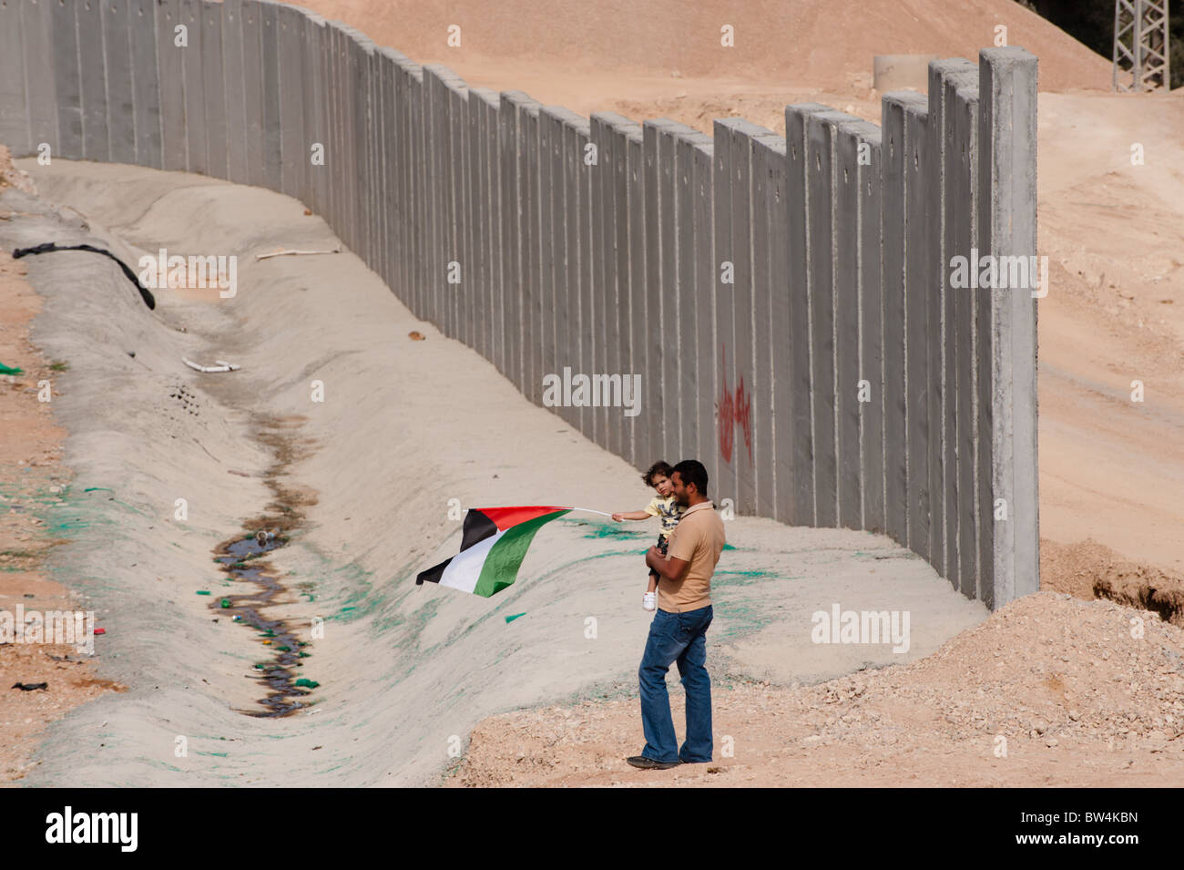 Father and daughter waving a Palestinian flag stand near the Israeli separation barrier being constructed in the West Bank. Stock Photo