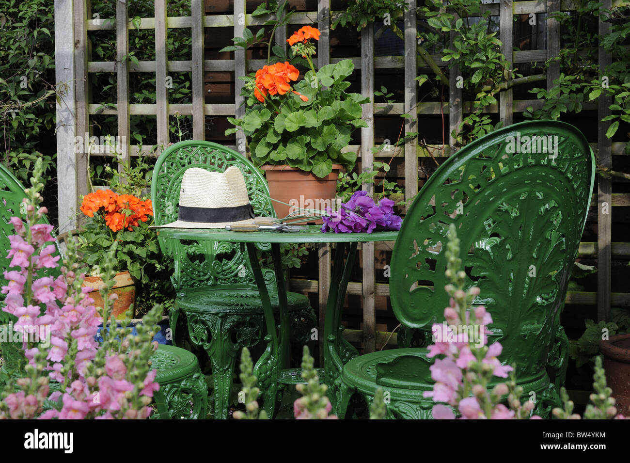 SUMMER SEATING AREA WITH GARDEN FURNITURE, POTTED GERANIUMS, ANTIRRHINUMS AND PANAMA HAT, NORFOLK, UK, JULY Stock Photo
