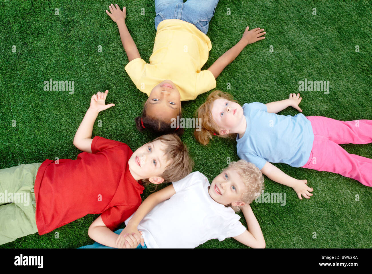 Image of little boys and girls lying on green grass and looking up Stock Photo