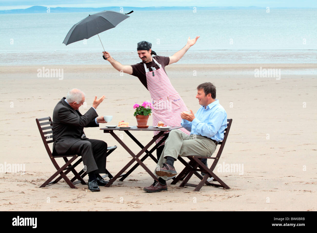 Waiter James Murray holds the rain off Scottish Culture Minister Jim Mather at Portobello Beach with Jonathan Bendit Stock Photo