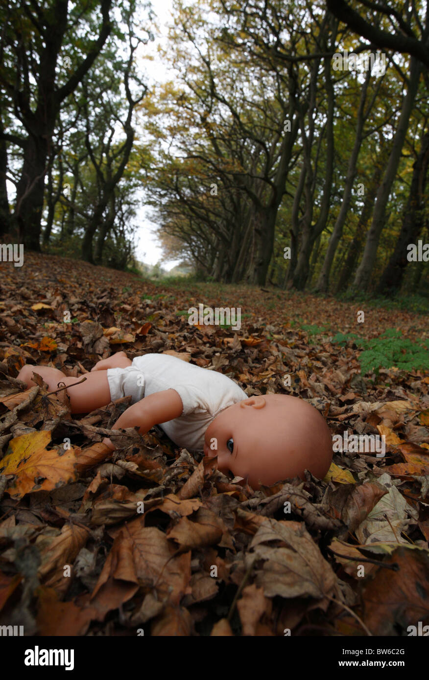 A childs doll face down on fallen leaves in the woods. Stock Photo