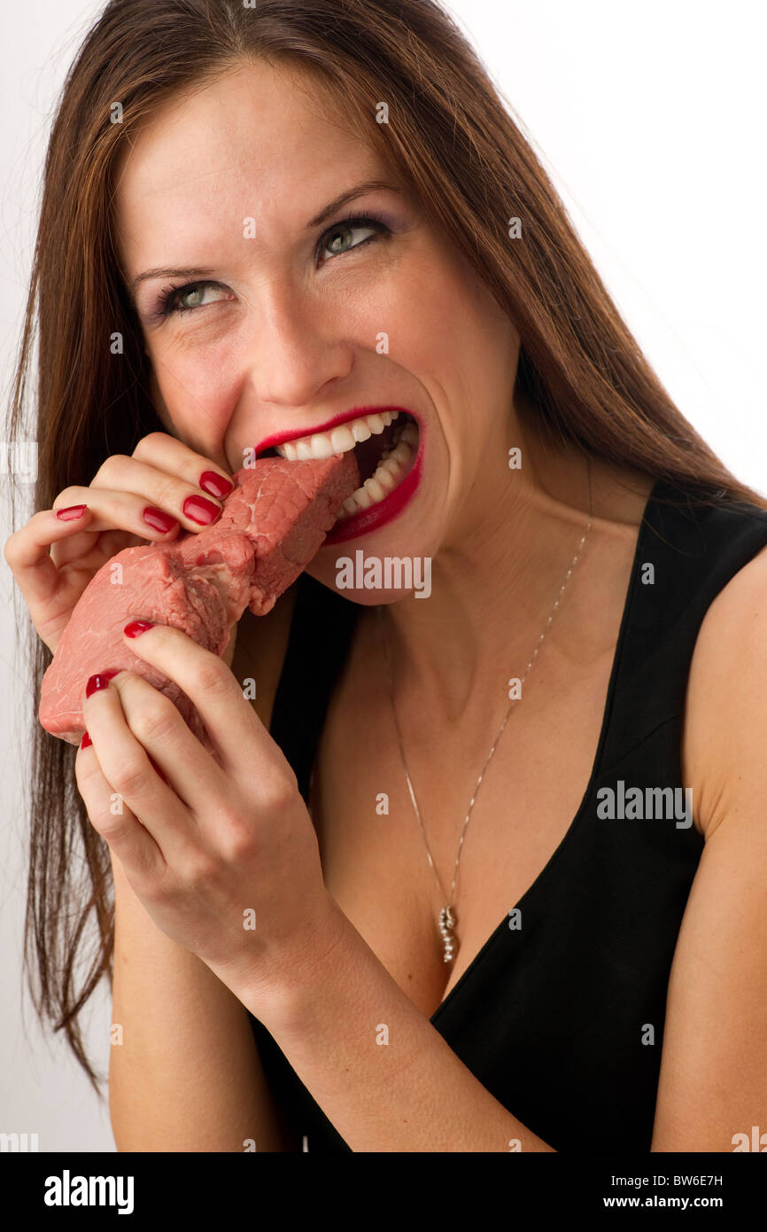 Beautiful Woman bites into a raw piece of Beef Stock Photo