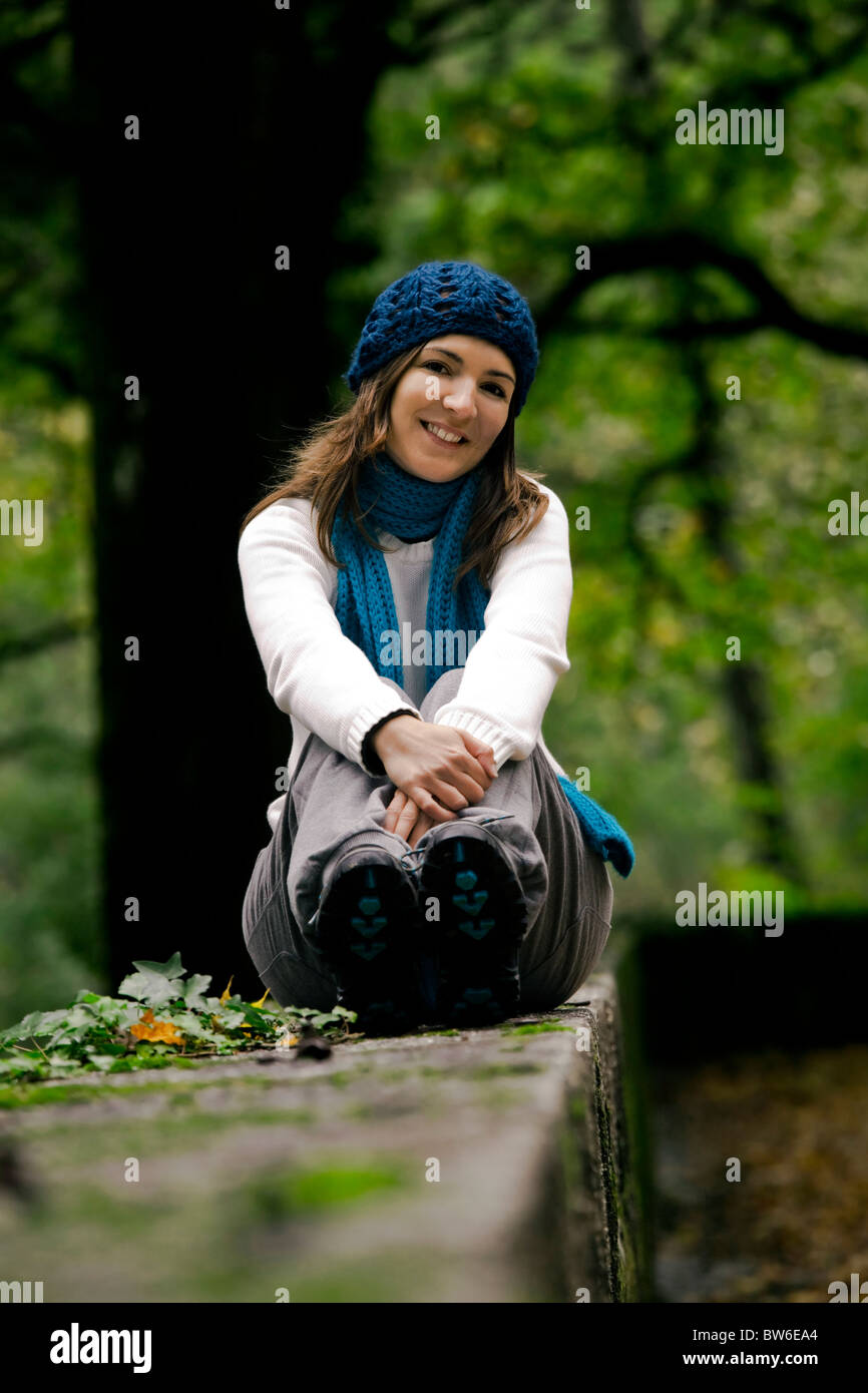 Outdoor portrait of a beautiful young woman sitting on a stonewall ...