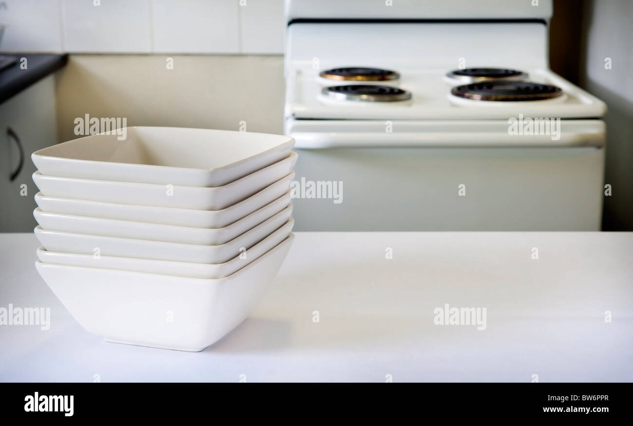 Contemporary square white bowls sit on the kitchen bench with stove behind Stock Photo