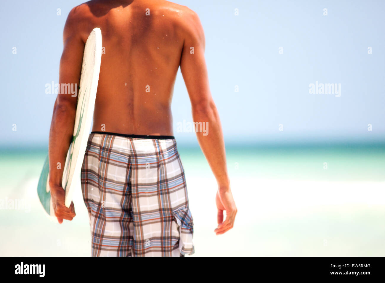 Young man carrying a skim board walking on a beach. Panama City Beach, Gulf Coast, Florida. Stock Photo