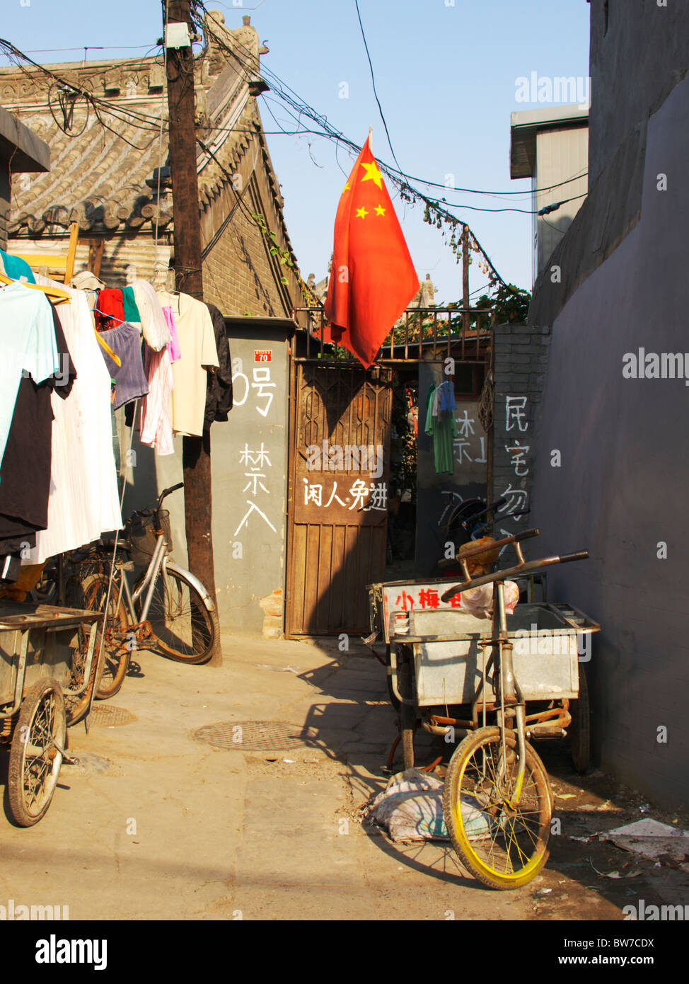 a bicycle and clothes hang outside a shanty house in the side streets of Beijing, while a Chinese flag flies at the back Stock Photo