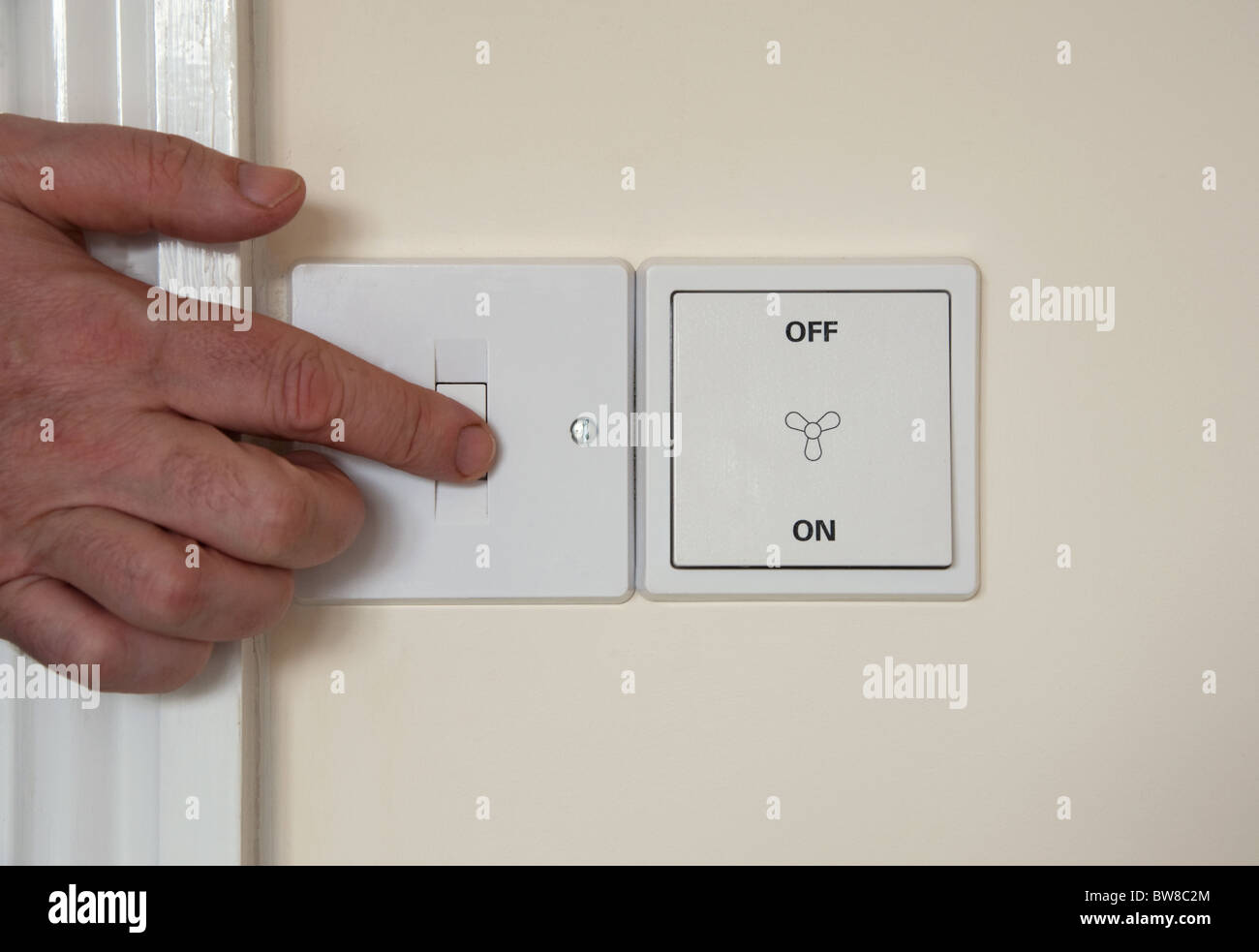 Modern, flush-mounted switches on a wall, one for a light, the other a ventilation fan. The photographer is pressing one switch. Stock Photo