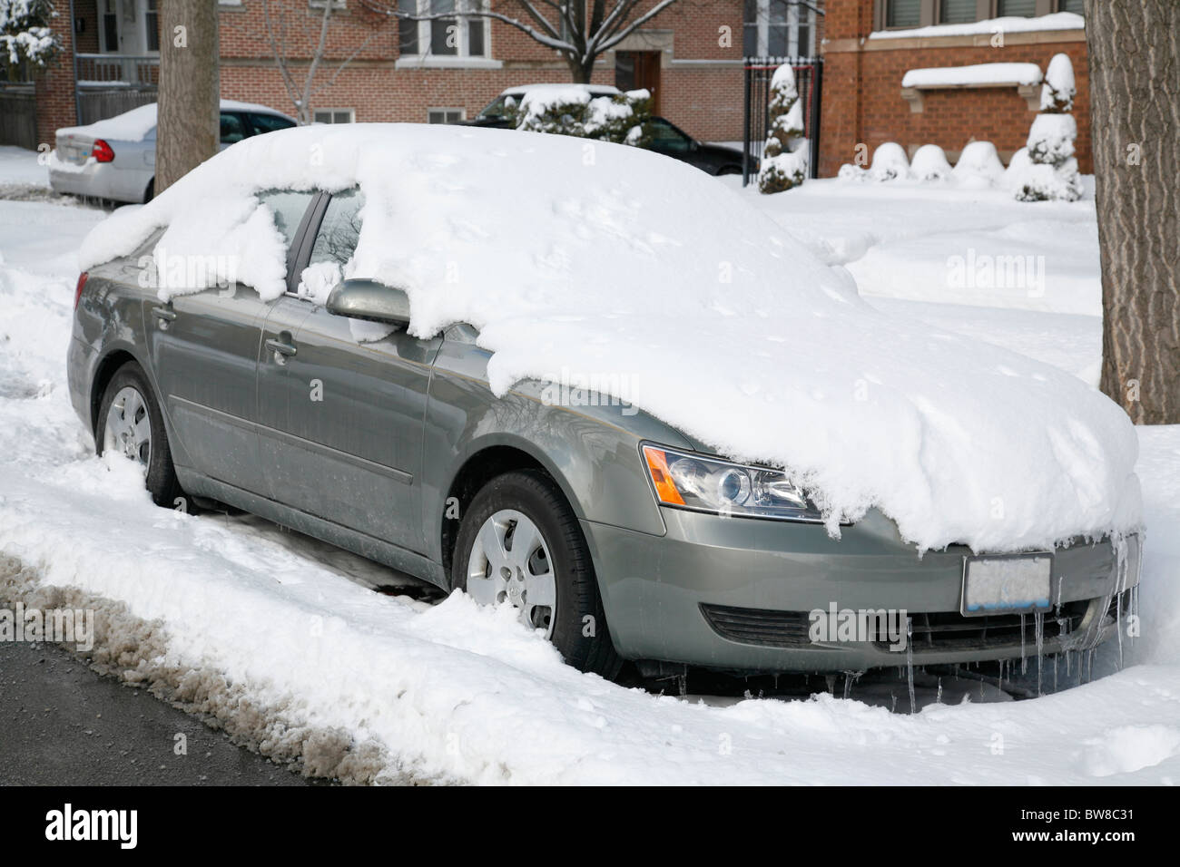 snow covers and surrounds a car parked on a city side street in winter ...