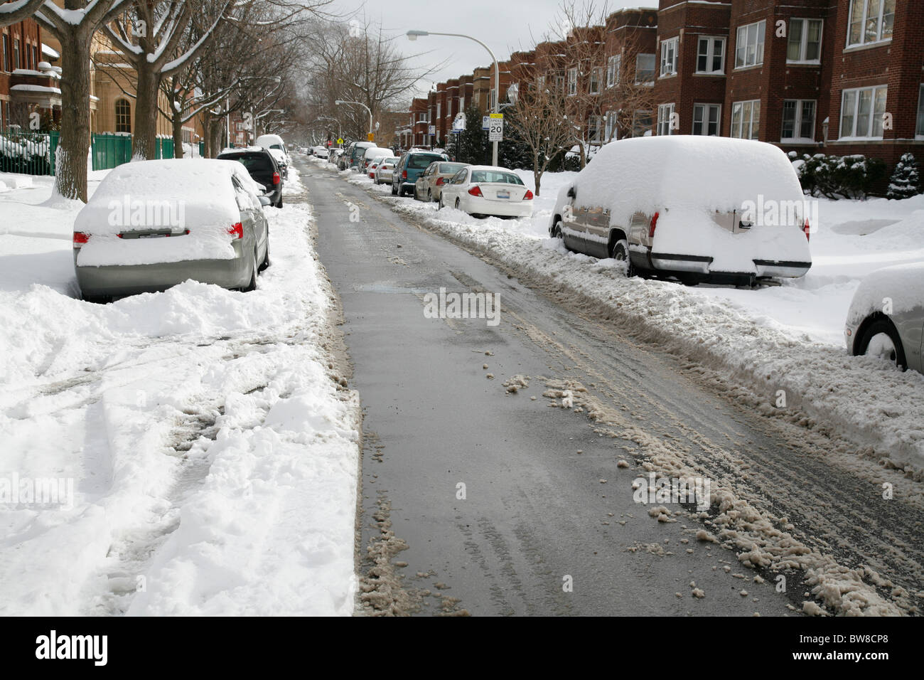 snow covers and surrounds cars parked on a plowed city street in winter ...