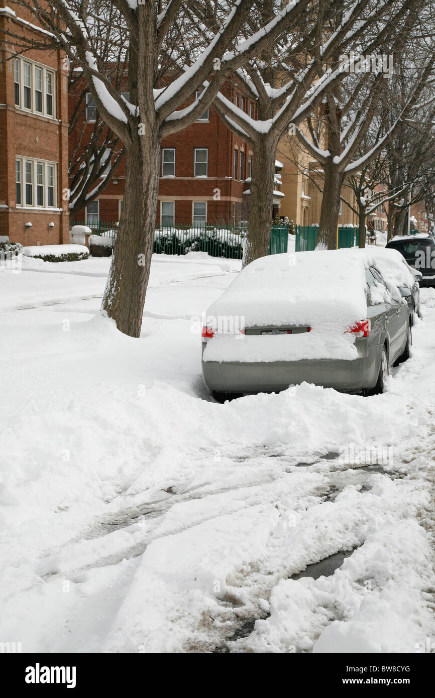 snow surrounds and covers cars parked on a plowed city side street in ...
