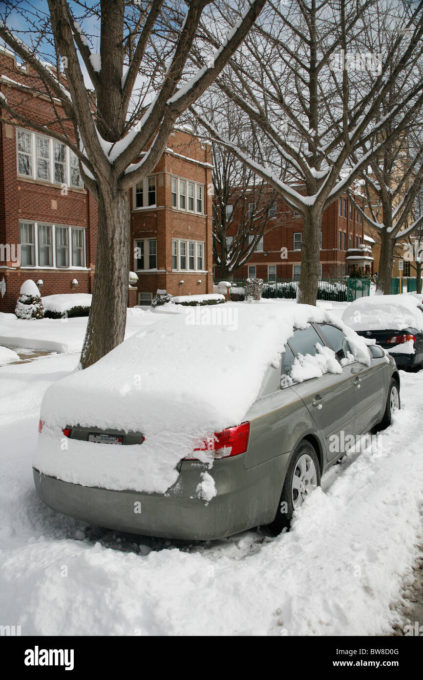 snow surrounds and covers cars parked on a plowed city side street in ...