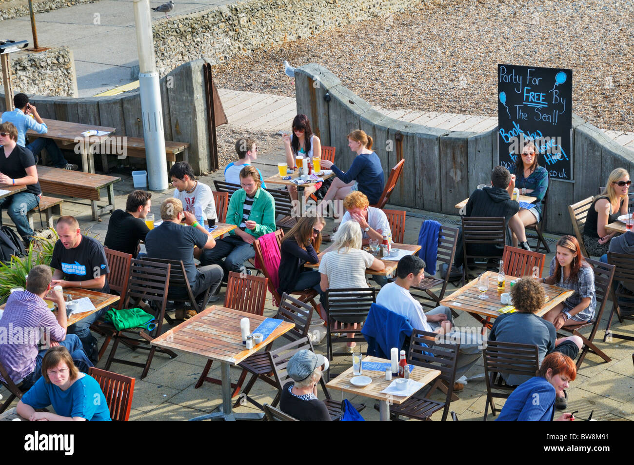 Peolpe relaxing with drinks at beachfront bar/cafe on Brighton beach, East Sussex, UK Stock Photo