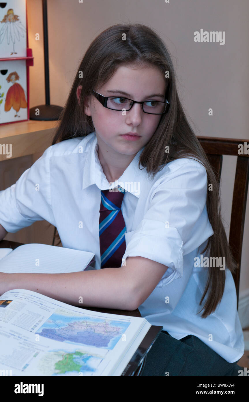 Young girl in school uniform wearing glasses doing her homework at the table Stock Photo