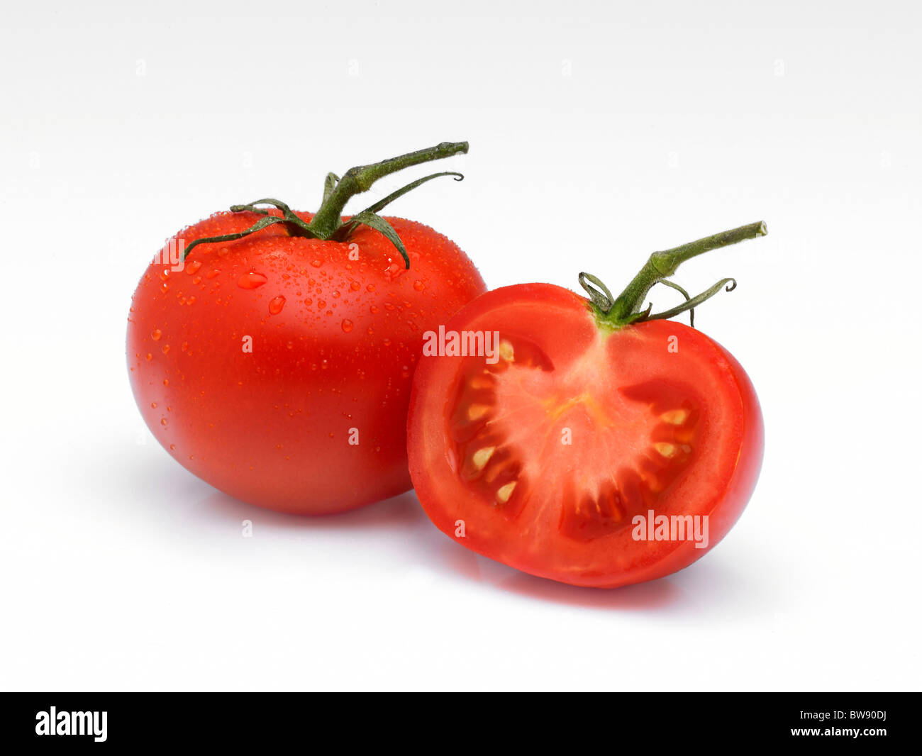 An arrangement of a whole Tomato and a half on a white background with water droplets and stalks. Stock Photo
