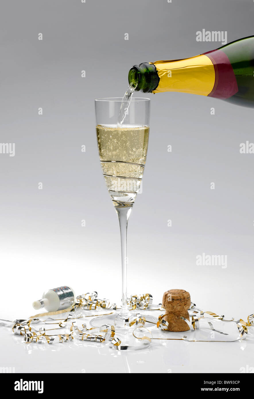 A single glass of champagne being poured from a bottle on a white background with popper and streamers Stock Photo