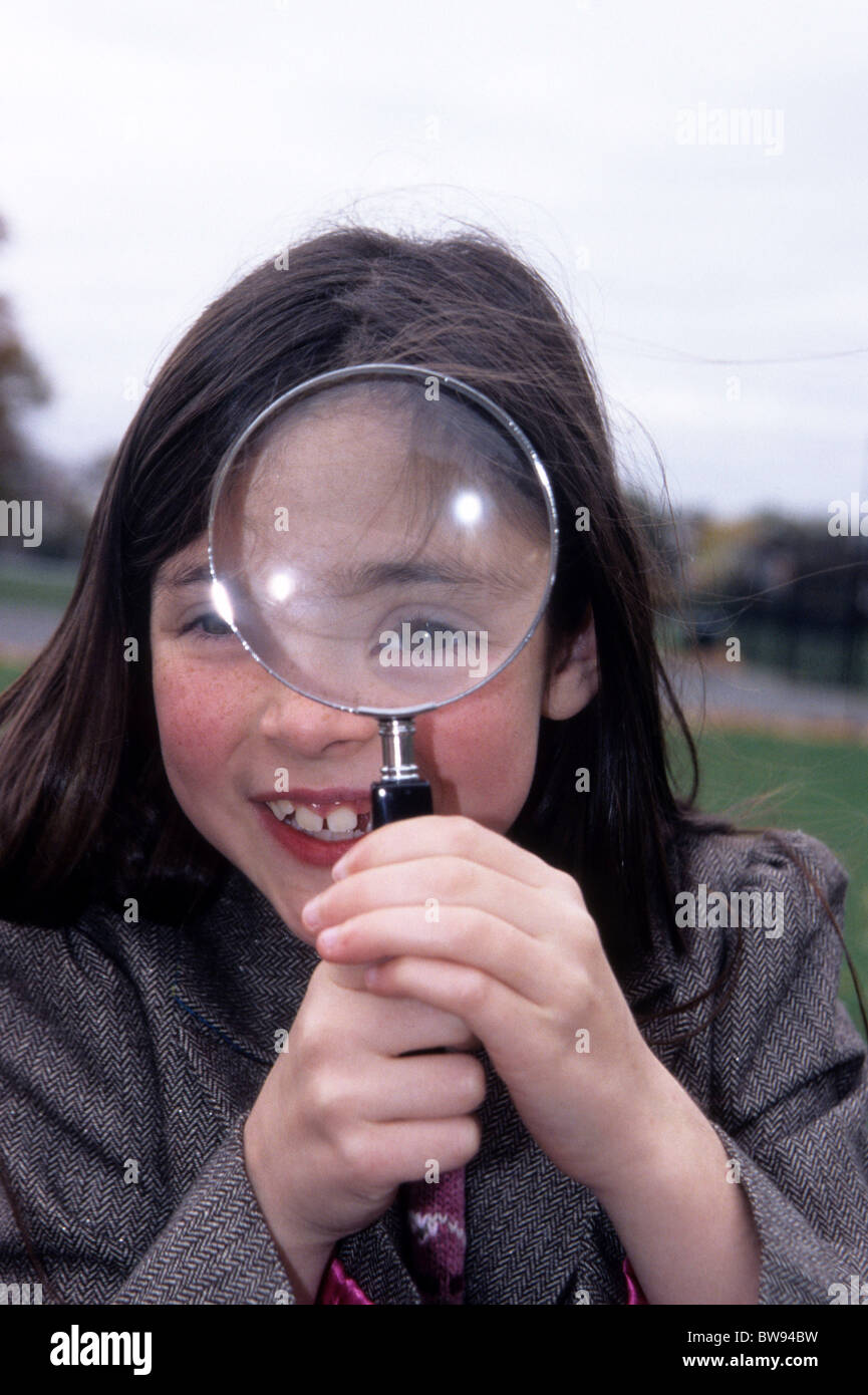 Pretty little girl holding a magnifying glass up to her eye. Stock Photo